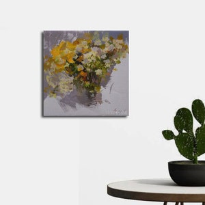 Op de afbeelding: Een olieverfschilderij op canvas toont een boeket gele en witte bloemen in een vaas. Het kunstwerk heeft een textuurrijke, impressionistische stijl met zichtbare penseelstreken. De achtergrond is zachtgrijs en het schilderij wordt op een witte muur getoond.