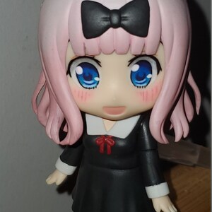 Op de afbeelding: Een anime-figuur met roze haar, een zwarte strik, een zwarte jurk met een witte kraag en een rode strik, en witte schoenen. Het figuur heeft blauwe ogen en roze wangen.