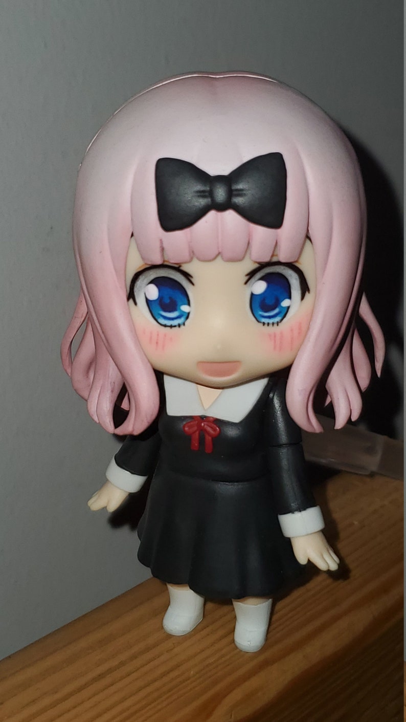 Op de afbeelding: Een anime-figuur met roze haar, een zwarte strik, een zwarte jurk met een witte kraag en een rode strik, en witte schoenen. Het figuur heeft blauwe ogen en roze wangen.
