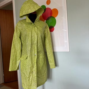 May include: A green raincoat with a hood and a small white button closure. The raincoat has a green and white polka dot pattern.