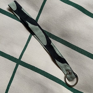 May include: A green and black camouflage fabric key chain with a silver metal ring.