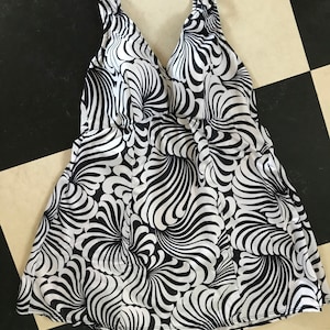 May include: Black and white swimsuit with a swirling pattern. The swimsuit has a V-neckline and a fitted bodice. The skirt portion of the swimsuit is full and flowing.