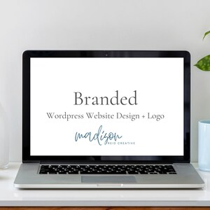 May include: A laptop displaying the words "Branded WordPress Website Design + Logo" with the name "madison reid creative" in a teal script. A white vase, a light blue mug, and a plant are on the white desk.