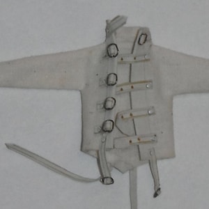 May include: A white straightjacket with long sleeves, metal closures, and straps. The jacket is laid out flat, with the sleeves extended to the sides. The metal closures are visible down the front of the jacket.