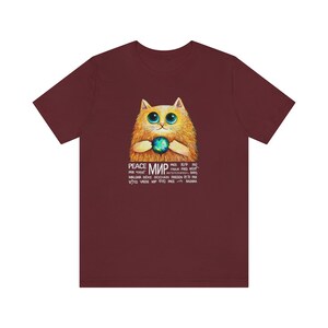 May include: A maroon t-shirt with a cartoon illustration of a cat holding a globe. The text "PEACE МИР" is printed on the shirt in multiple languages.