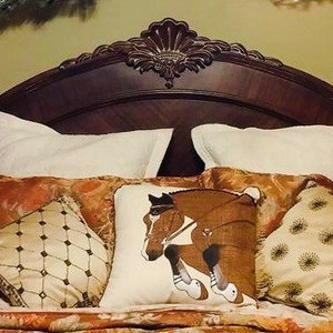 May include: A bed with a brown headboard and a white, brown, and gold patterned bedding set. The bedding includes a pillow with a horse jumping over a fence.