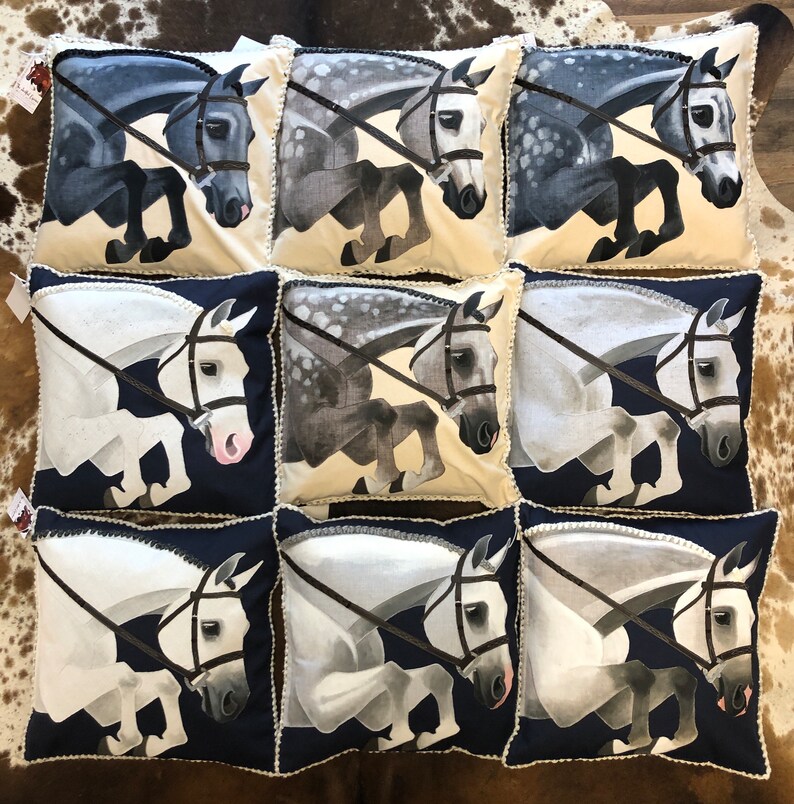 May include: Nine decorative throw pillows featuring a white background and a horse jumping over a fence. The horses are all different colours, including grey, white, and black. The pillows have a white trim and a blue background.