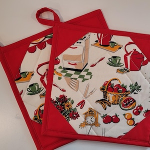 May include: Two square quilted pot holders with a red border and hanging loop. The center fabric features a vintage kitchen scene with a stove, teapot, and fruit basket. The pot holders are designed to protect hands from heat.