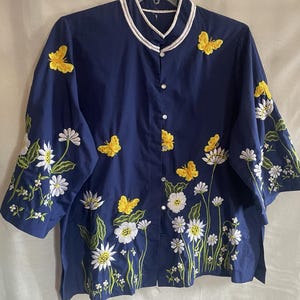 May include: A navy blue button-up shirt with white and yellow embroidered flowers and butterflies.