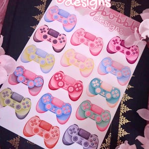 May include: Sheet of colorful video game controller stickers in shades of pink, blue, yellow, and green. The stickers have a watercolor effect and the text "bekkybubble designs" is at the top.