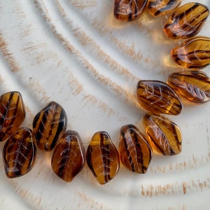 May include: A strand of brown glass leaf beads with a textured surface. The beads are strung on a clear thread.