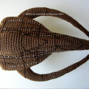 May include: A brown crocheted amigurumi toy shaped like a head with two long, curved horns. The toy has a detailed design with white stitching and black embroidery.