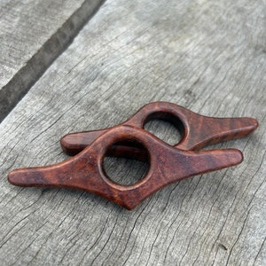 Può includere: Due ferma libri in legno di colore marrone scuro. I ferma libri hanno la forma di una lacrima con un foro rotondo al centro. I ferma libri sono su una superficie di legno.