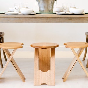 May include: Three wooden folding stools with a natural finish. The stools have a round seat and a criss-cross base.