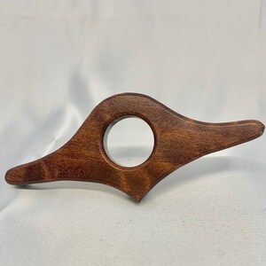 Puede incluir: Un marcapáginas de madera marrón oscuro con un diseño curvo único y un recorte circular en el centro.