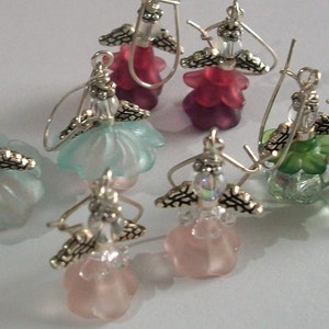 May include: Six pairs of dangle earrings with a silver angel wing design. The earrings feature a variety of colors including pink, green, blue, and clear. The earrings are made of glass and metal.