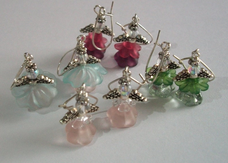 May include: Six pairs of dangle earrings with a silver angel wing design. The earrings feature a variety of colors including pink, green, blue, and clear. The earrings are made of glass and metal.