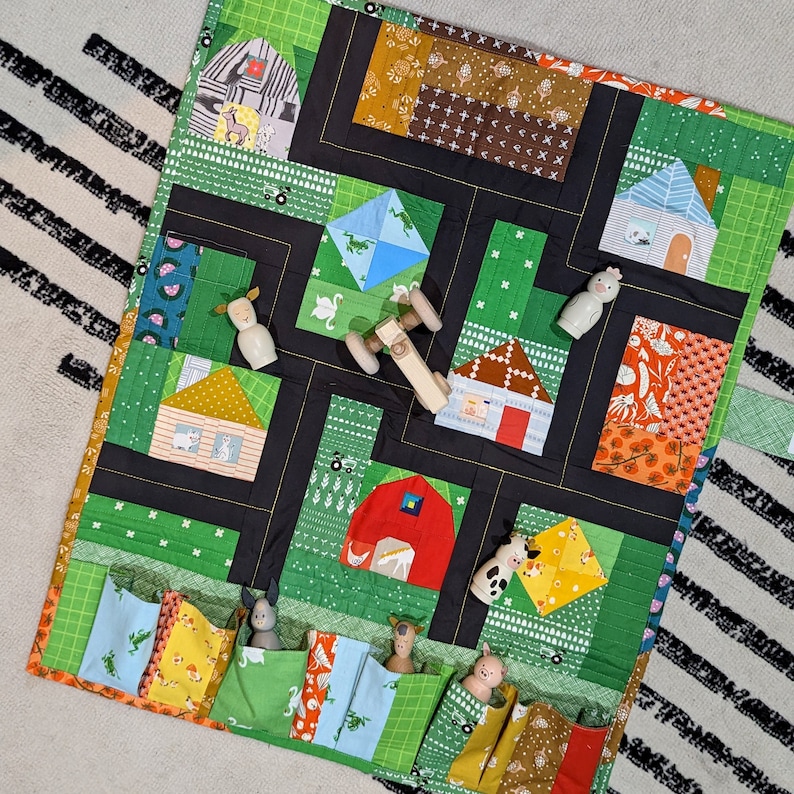 Op de afbeelding: Een groene en zwarte stoffen speelmat met een boerderijthema. De mat heeft zakken aan de zijkanten en toont verschillende afbeeldingen van dieren en boerderijen. De mat is perfect voor kinderen om op te spelen en te leren over boerderijdieren.