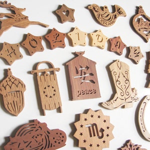 Peut inclure: Une collection d'ornements en bois sculpté avec des formes variées, dont des étoiles, un renne, un oiseau et une botte de cowboy. Les ornements sont en bois brun clair et foncé, avec des motifs découpés. Certains ornements ont du texte.