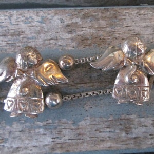 May include: Silver-toned angel bracelet featuring detailed angel figures with wings and heart-shaped accents. The bracelet includes small, round beads and a delicate chain, perfect for adding a touch of charm to any outfit.