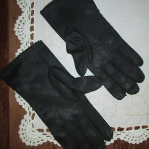 May include: A pair of black leather gloves with a stitched design. The gloves are laid out flat on a white crocheted surface.