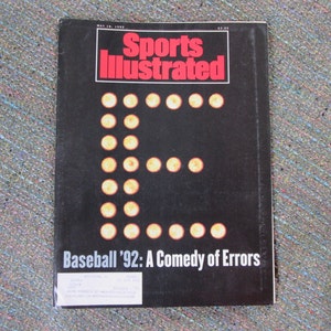 May include: A black and white magazine cover for Sports Illustrated with the text "Baseball '92: A Comedy of Errors" and a large letter "E" made of yellow dots.