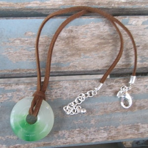 May include: A green and white jade pendant with a brown suede cord and silver chain and clasp.