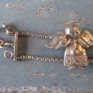 May include: Silver-toned angel bracelet with a toggle clasp. The bracelet features small angel charms with detailed wings and heart-shaped accents on their gowns. The chain is a delicate box chain style.