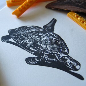 May include: Black and white line art print of a turtle with its head turned to the side. The turtle is facing the right side of the image. The print is on a white background.