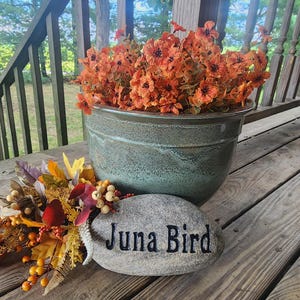 May include: A green ceramic planter with orange flowers and a gray stone with the text "Juna Bird" on it.