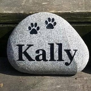 May include: A gray stone with two black paw prints and the name "Kally" written in black lettering.
