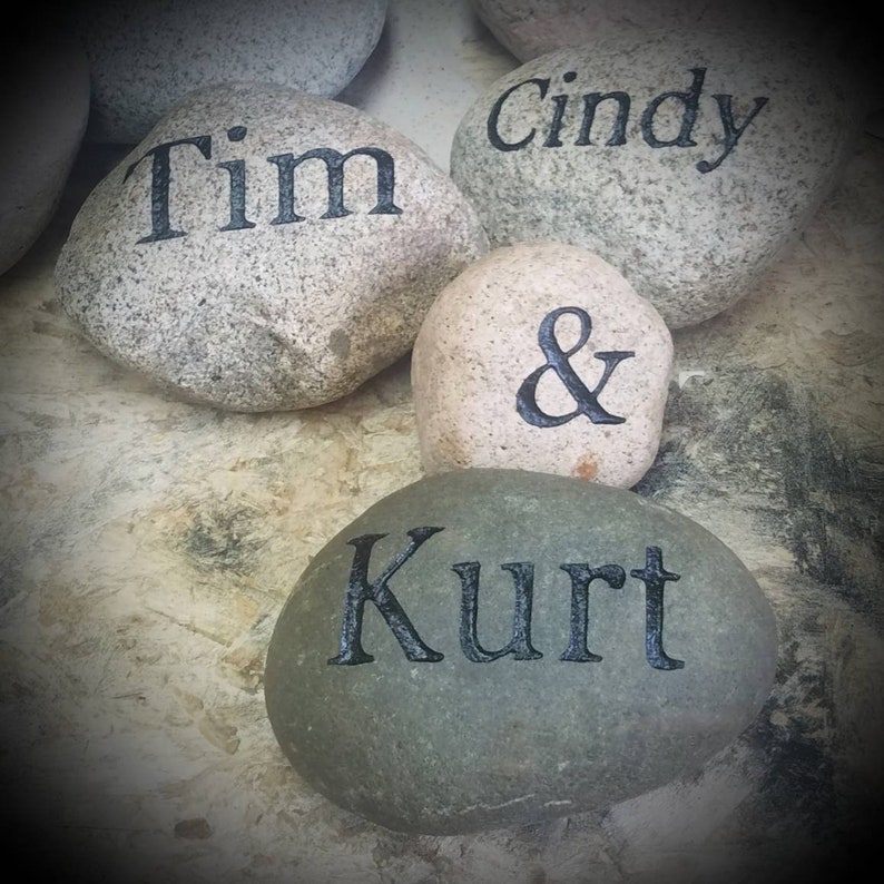 May include: Four gray and white stones with black lettering. The stones are engraved with the names "Tim", "Cindy", "&", and "Kurt".