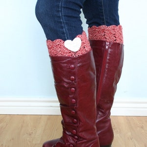 May include: Burgundy leather boots with a button detail on the side. The boots are worn with a pair of jeans and a crocheted leg warmer with a white heart.