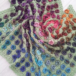Könnte beinhalten: Eine gehäkelte Decke mit einem Spiralmuster aus bunten Blumen. Die Decke ist aus verschiedenen Grüntönen, Lila, Blau, Rosa und Orange gefertigt.