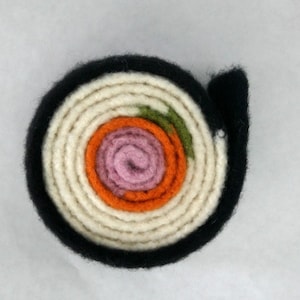 May include: A felt sushi roll with a black outer layer, white rice, orange and pink fish, and green seaweed.
