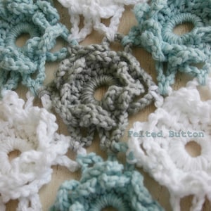 May include: Close-up of a crocheted doily with a repeating pattern of white, gray, and light blue flowers. The doily is made with a delicate, lacy stitch.