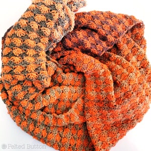 May include: A crocheted scarf in shades of orange and brown, with a textured, woven pattern. The scarf is folded and arranged in a circular shape.