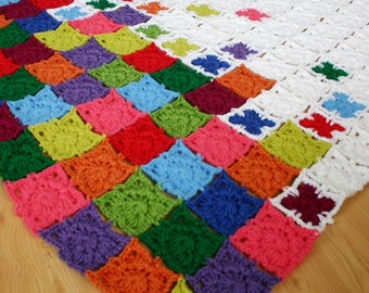 Puede incluir: Una manta de crochet colorida con un patrón de arcoíris. La manta está hecha de cuadrados de diferentes colores, incluyendo rojo, naranja, amarillo, verde, azul, índigo y violeta. La manta está colocada sobre un suelo de madera.