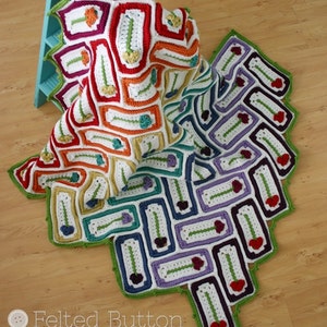 May include: A colorful crochet blanket with a rainbow pattern of squares and flowers. The blanket is folded in half and draped over a blue wooden step stool. The text "Felted Button" is visible in the lower left corner of the image.