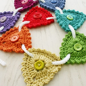 May include: A rainbow crochet garland with colorful buttons. Each heart-shaped crocheted piece is connected with white string.