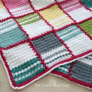 May include: A crocheted blanket with a patchwork design in shades of white, pink, yellow, green, and gray. The blanket is edged with a pink crocheted border.