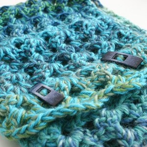 May include: A teal, blue, and green crocheted cowl with two black plastic toggles.