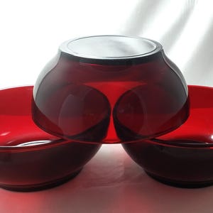 May include: Three red glass bowls, one larger bowl stacked on top of two smaller bowls.