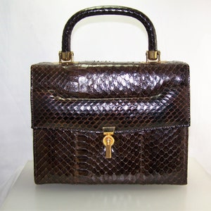May include: A brown snakeskin handbag with a gold-toned handle and clasp.