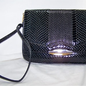 May include: A black snakeskin clutch purse with a gold clasp and a long strap.