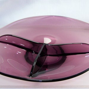 May include: A purple glass serving dish with three divided sections. The dish has a wavy edge and a slightly raised center.