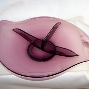 May include: A purple glass serving dish with a divided center section. The dish has a wavy edge and a smooth, glossy finish.