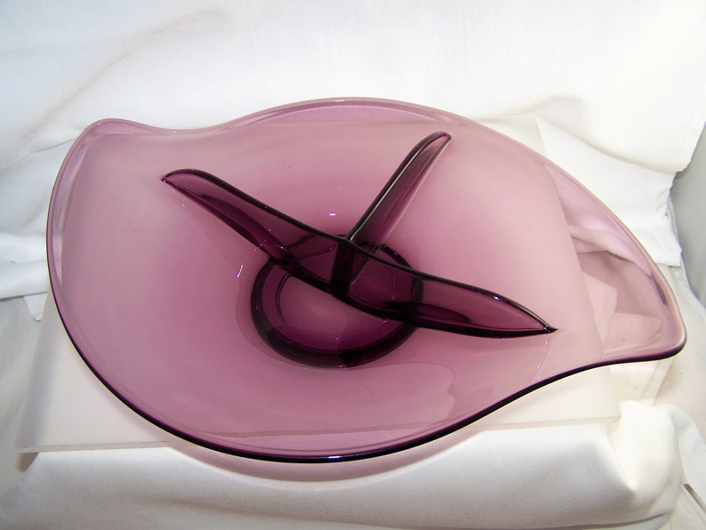 May include: A purple glass serving dish with a divided center section. The dish has a wavy edge and a smooth, glossy finish.