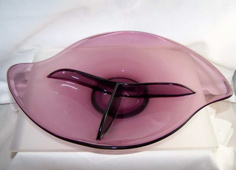 May include: A purple glass serving dish with three divided sections. The dish has a wavy, organic shape.
