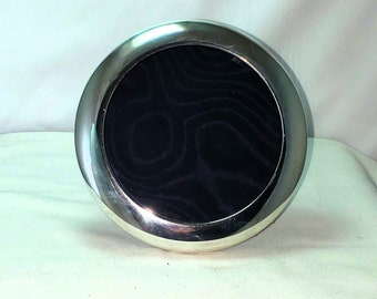 May include: A round silver picture frame with a black velvet backing.